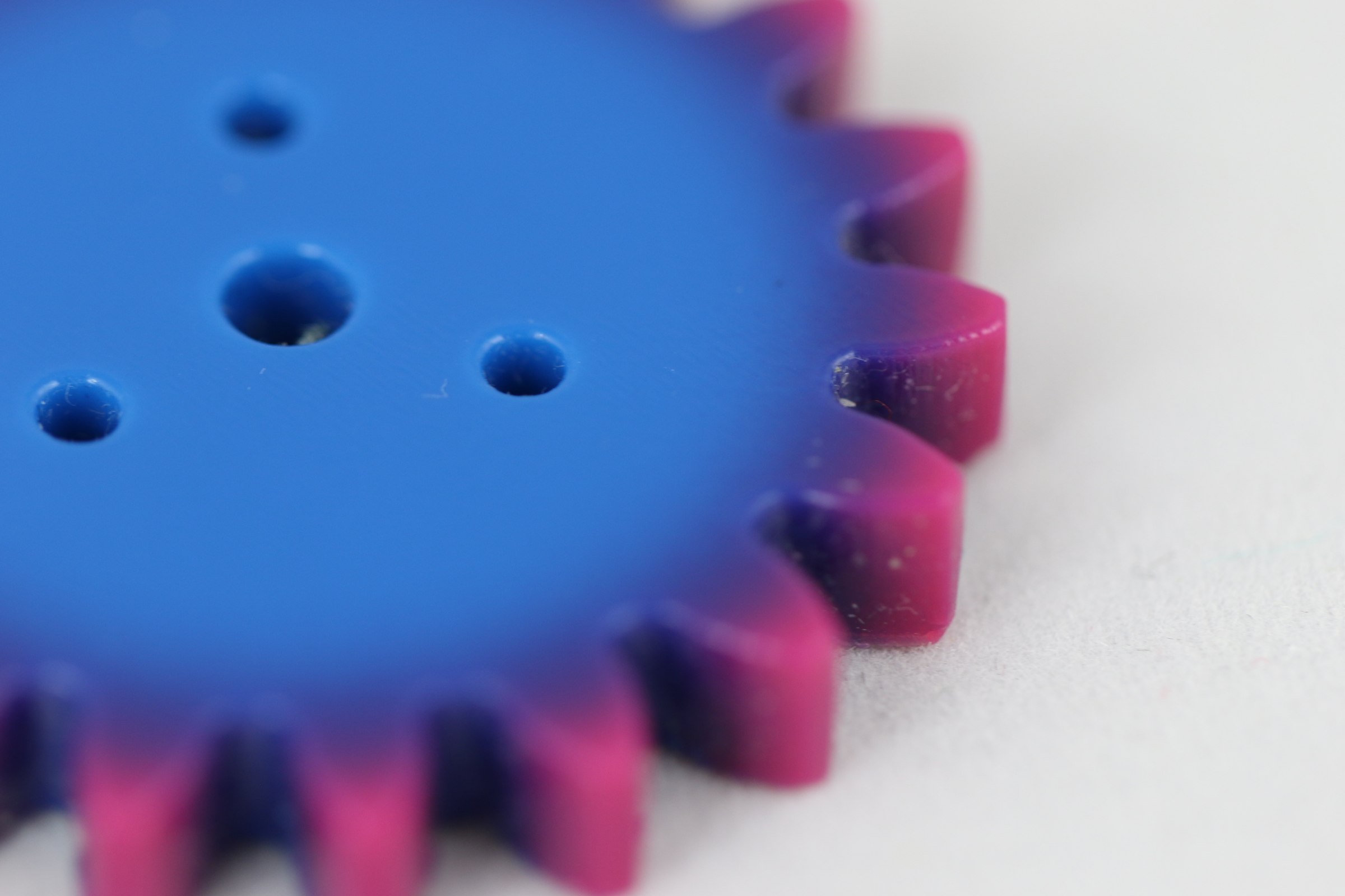 Close-up of a printed gear, blue in the middle and shading to magenta at the teeth.