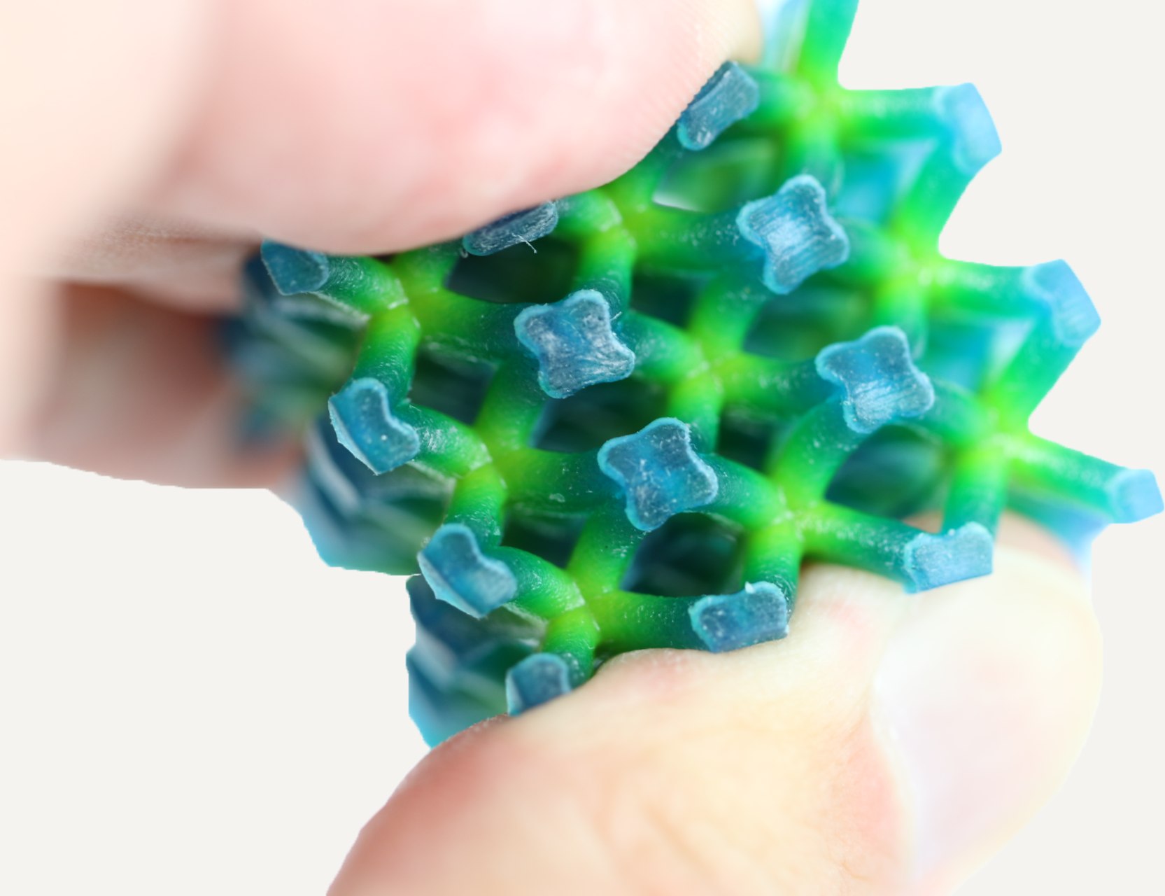 The printed green and blue lattice compressed between two fingers.
