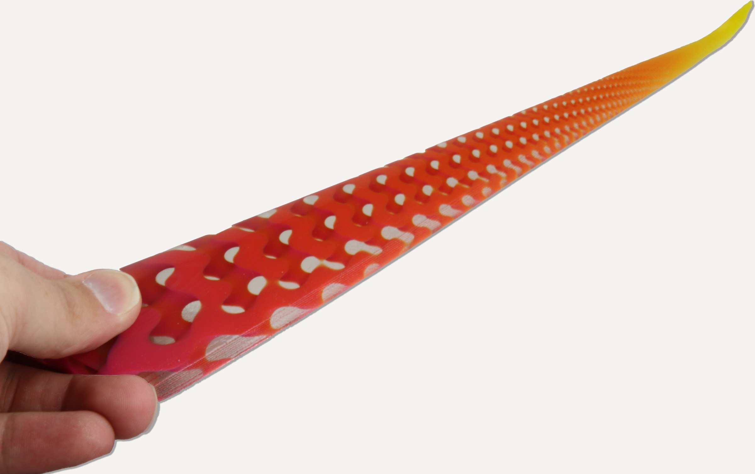 A printed red and yellow wing with gyroid openings, held at its root.